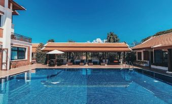 a large swimming pool with a covered area and lounge chairs is surrounded by trees at Content Villa Chiangmai