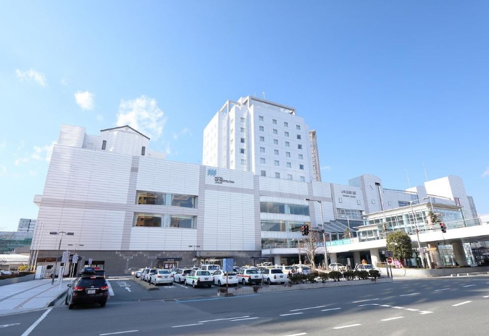 a white building with a large glass facade is surrounded by cars and people on a street at Hotel Metropolitan Yamagata