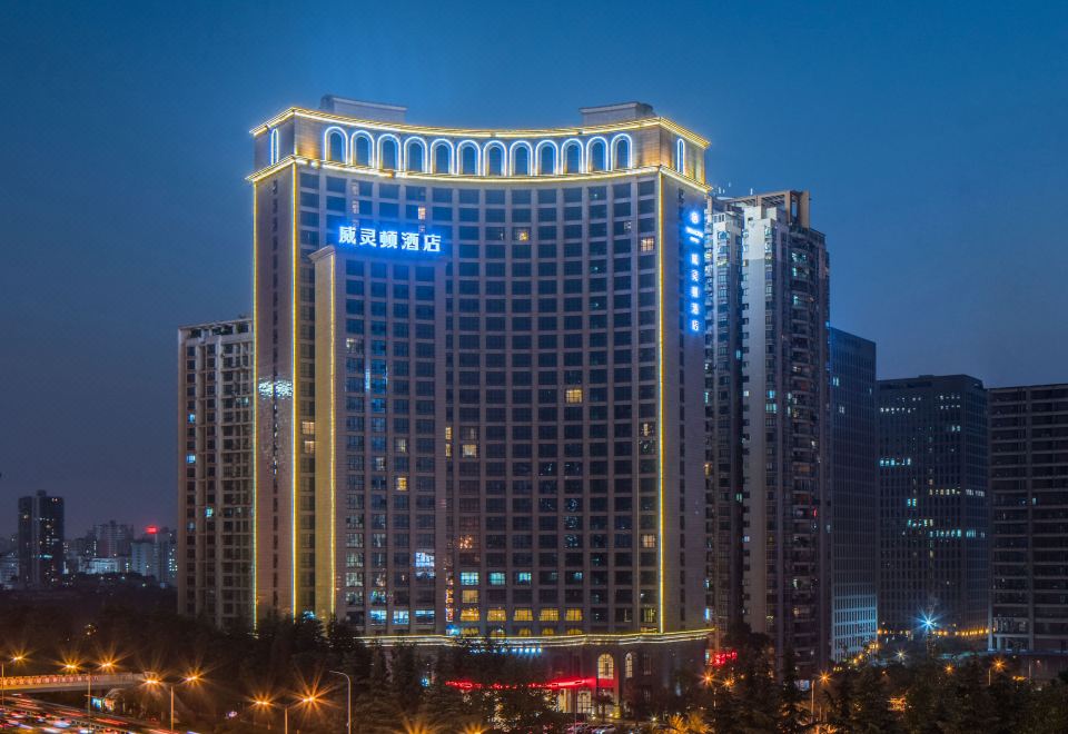 a tall building with a blue and white sign is lit up at night , surrounded by cars at Wellington Hotel