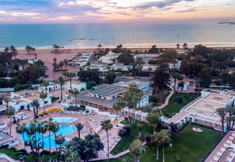 a resort with a pool and ocean view is shown from an aerial perspective , with palm trees in the foreground at Allegro Agadir