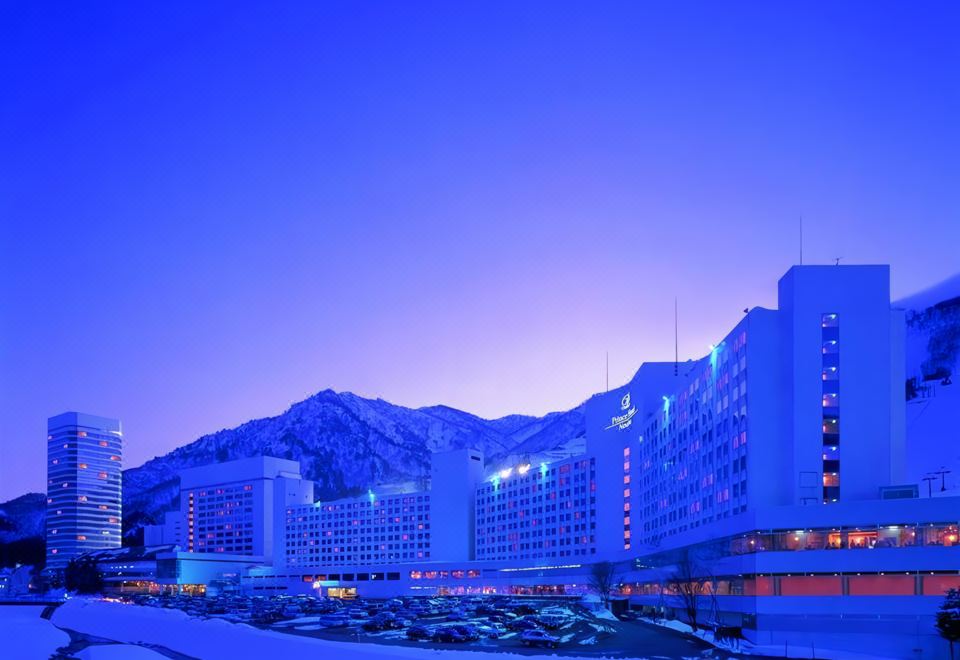 a large hotel is lit up at night , with a mountain in the background and snow on the ground at Naeba Prince Hotel