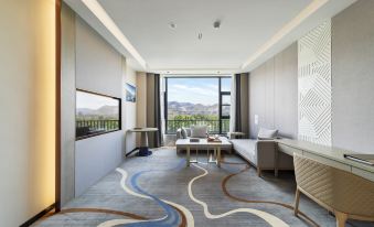 a modern living room with a large window and sliding glass door , featuring a dining area , couch , and television at xizang hotel  （Norbulingka shop)