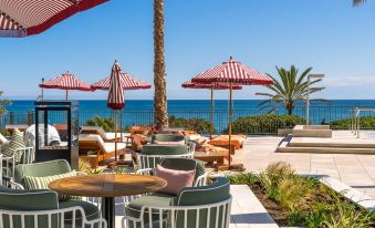 an outdoor dining area near the beach , with several chairs and tables arranged for guests to enjoy a meal at El Fuerte Marbella