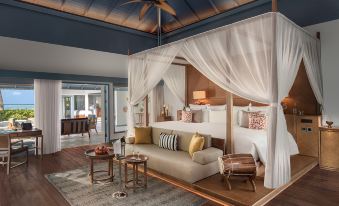 a luxurious bedroom with a canopy bed , a couch , and a dining table in the room at Raffles Maldives Meradhoo Resort