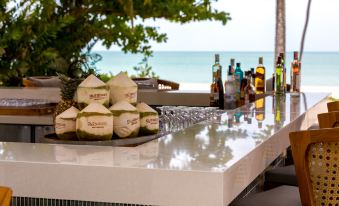 a bar with a table full of bottles and coconuts , as well as a view of the ocean in the background at Outrigger Khao Lak Beach Resort