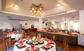 a large , well - lit dining room with multiple tables set for a meal , including plates , cups , and utensils at The Imperial Narathiwat Hotel