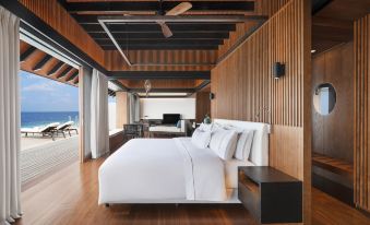 a large bed with white linens is in a room with wooden walls and floors at The Westin Maldives Miriandhoo Resort