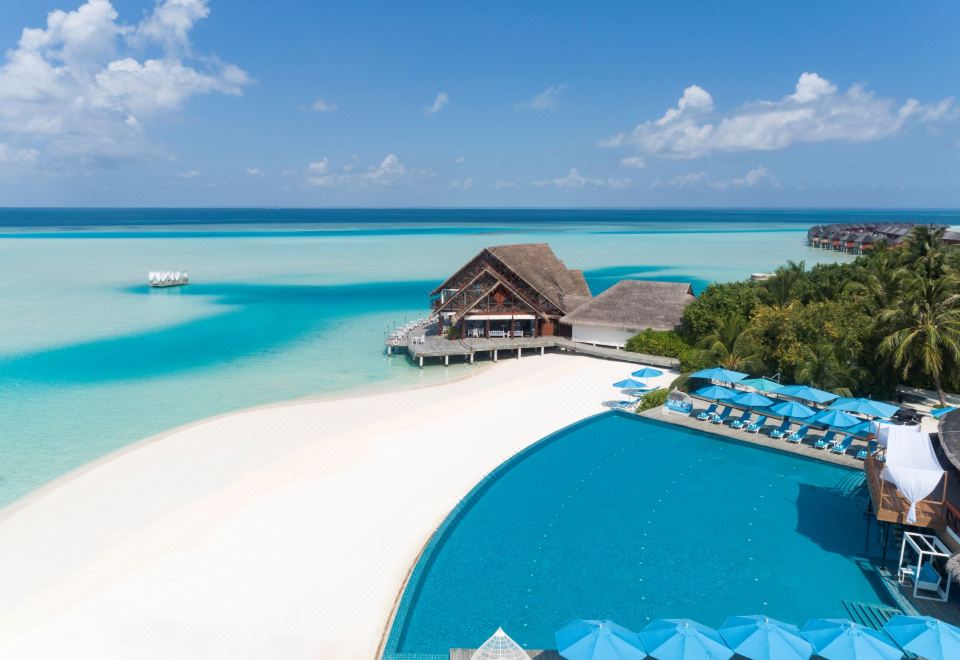 a resort with a large pool surrounded by lounge chairs and umbrellas , as well as a sandy beach in the background at Anantara Dhigu Maldives Resort - Special Offer on Transfer Rates for Summer 2024