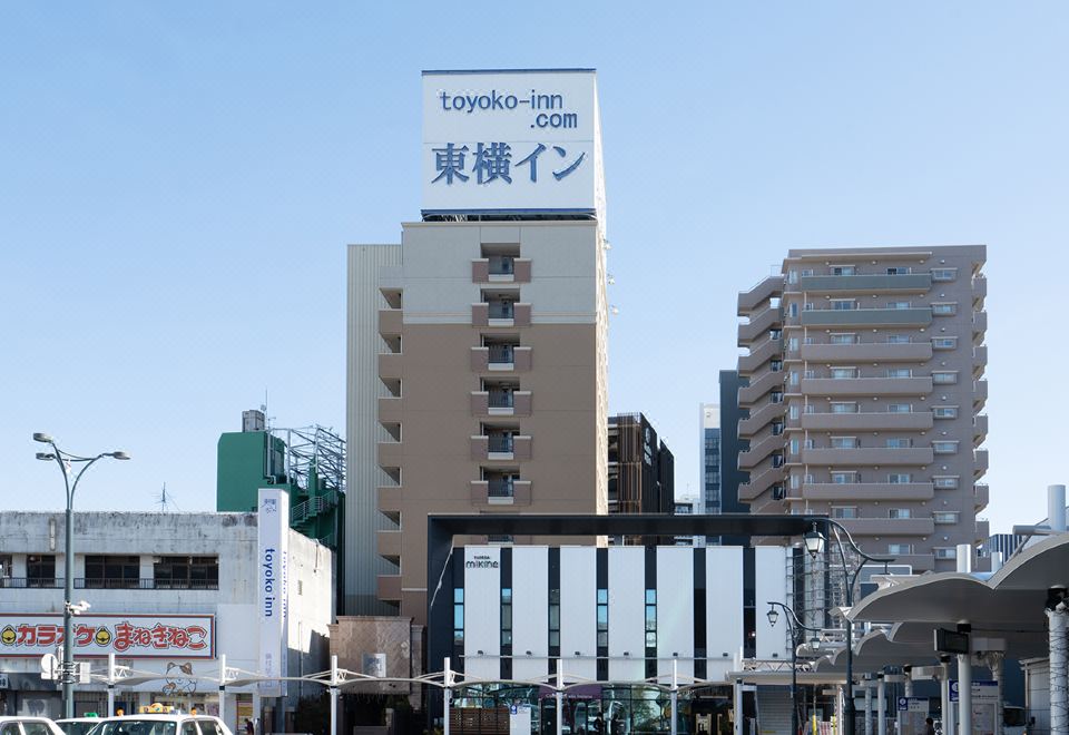 a city street with a tall building and a sign for the toyoko - inn com at Toyoko Inn Shizuoka Fujieda Eki Kita Guchi