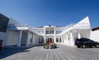 a large white building with columns and a parking lot in front of it , under a clear blue sky at Capital O 1888 Griya RW Family Guest House
