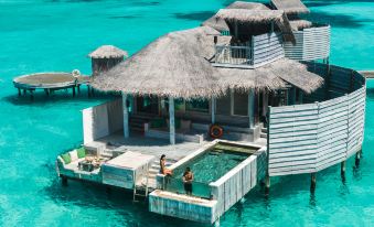 a floating wooden house on stilts in the ocean , surrounded by clear blue water and surrounded by lush green vegetation at Six Senses Laamu