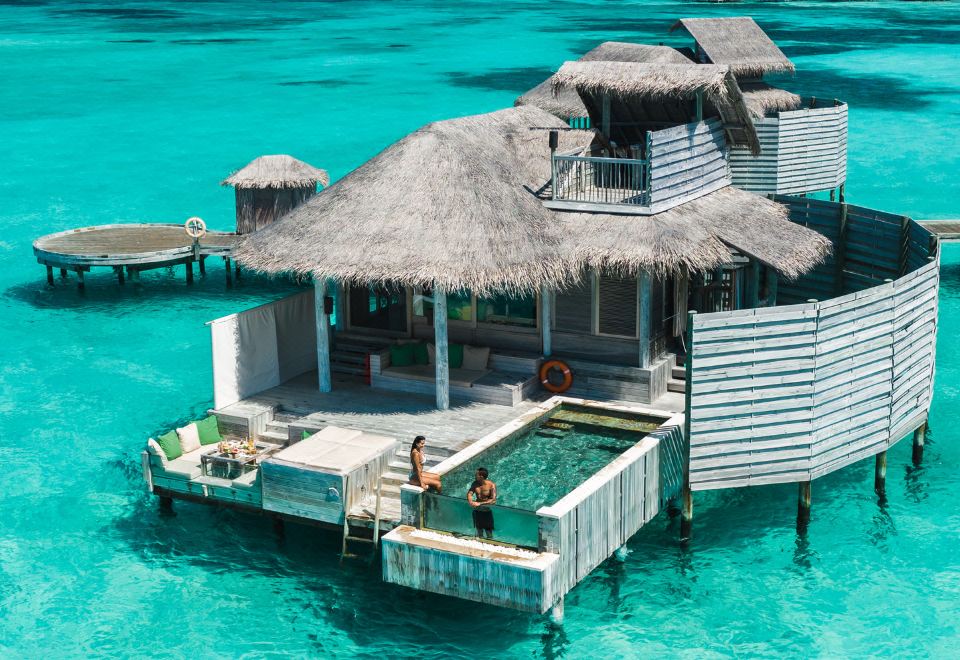 a floating wooden house on stilts in the ocean , surrounded by clear blue water and surrounded by lush green vegetation at Six Senses Laamu