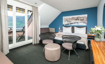a modern hotel room with a large bed , black leather chairs , and a view of the ocean at Seehotel Kastanienbaum