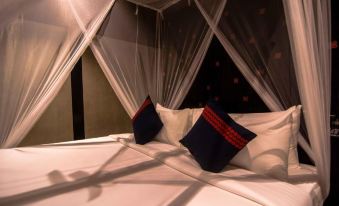 a bed with a white sheet and two blue and red pillows is covered by a canopy at Santani Wellness Kandy