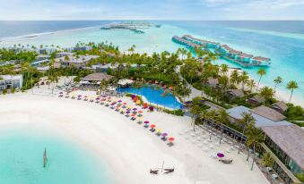 a beautiful beach with white sand , clear blue water , and various lounge chairs and umbrellas surrounding a resort at Hard Rock Hotel Maldives