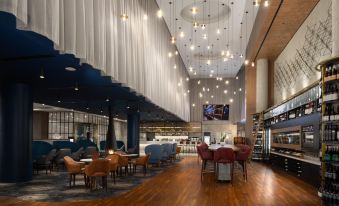 a modern lounge area with wooden floors , large windows , and hanging lights , featuring a variety of chairs and tables at Oval Hotel at Adelaide Oval, an EVT hotel