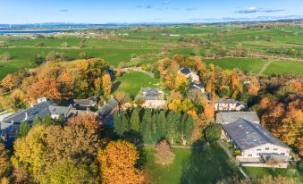 aerial view of a large house surrounded by trees and grass , with a lake in the background at Thurnham Hall