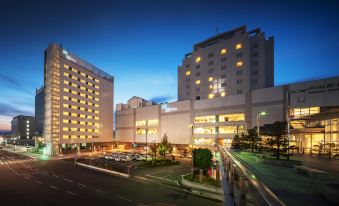 a modern city street at dusk , with multiple buildings and cars visible , including the hilton , lit up by lights at Hotel Metropolitan Yamagata