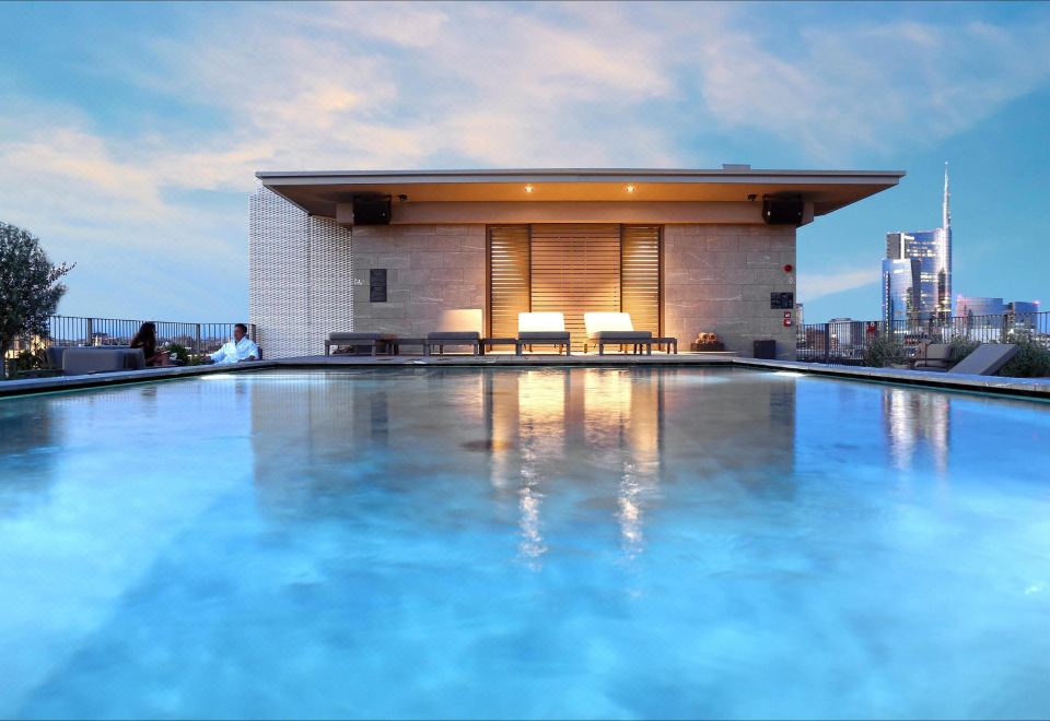 a large swimming pool surrounded by lounge chairs and tables , with a building in the background at Hotel Viu Milan, a Member of Design Hotels