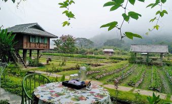 a table with a floral tablecloth is set on a terrace , overlooking a lush green garden and houses at Lhongkhao Samoeng by Chi Villa