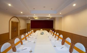 a long table with white tablecloths and chairs is set up in a room with a red curtain at The Imperial Narathiwat Hotel