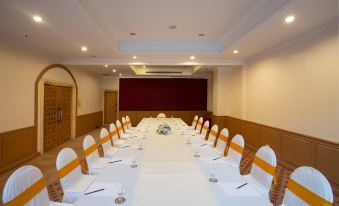 a long dining table is set with white tablecloths and orange place mats , ready for a large group of people at The Imperial Narathiwat Hotel