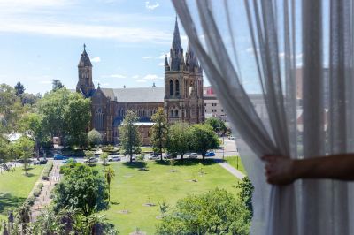 a woman standing in front of a large window , looking out at a beautiful view of a church and its surrounding landscape at Oval Hotel at Adelaide Oval, an EVT hotel