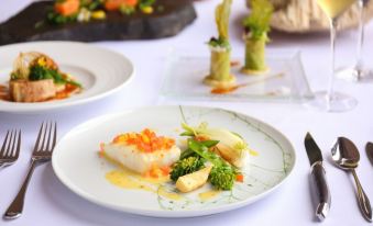 a white plate with a dish containing broccoli and carrots , garnished with sauce and served on a table at Sankara Hotel & Spa Yakushima