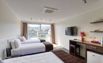 a modern hotel room with two beds , a desk , and a tv , as well as a balcony offering views of the surrounding landscape at Marsden Lake Resort Central Otago
