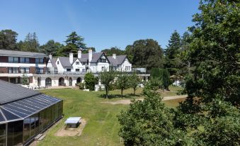 a large house with a green lawn in front of it , surrounded by trees and grass at Hilton Cobham