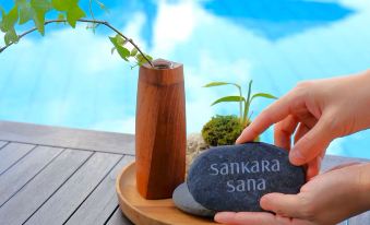 a woman is holding a rock in her hand , next to a vase with plants and a vase with a plant , near a swimming pool at Sankara Hotel & Spa Yakushima