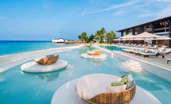 a large pool surrounded by lounge chairs and umbrellas , with people enjoying their time in the water at The Westin Maldives Miriandhoo Resort