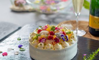 a cake with a white glaze and various fruits on top is placed next to a glass of champagne at Sankara Hotel & Spa Yakushima