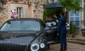 a man in a suit is holding an umbrella near a black car with its door open at L'Hotel de Beaune