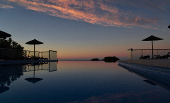 a large swimming pool surrounded by lounge chairs and umbrellas , with the sun setting in the background at Vila Alba Resort