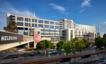 a large building with a pink advertisement on the side and trees in front of it at PARKROYAL Melbourne Airport