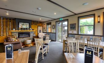 a modern , well - lit restaurant with wooden furniture and green signage , featuring large windows offering views of the outside at Marsden Lake Resort Central Otago