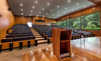 a large auditorium with wooden chairs and a wooden podium , surrounded by windows and a forest view outside at Vidago Palace