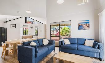 a modern living room with two blue couches , wooden coffee table , and large windows overlooking a patio at Amalfi Resort