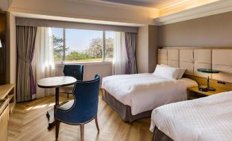 a hotel room with two beds , a dining table , and a chair , all situated near a window at Kawana Hotel