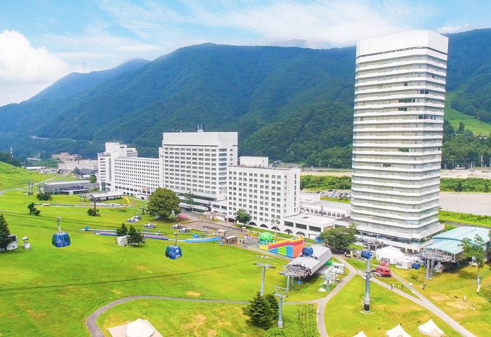 a large building with a playground in front of it and mountains in the background at Naeba Prince Hotel