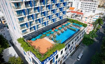 a large building with a blue swimming pool on its roof , surrounded by greenery and cars parked nearby at TUI BLUE Nha Trang