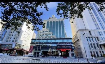 a large white building with a large statue on top is shown in front of trees at Victoria International Hotel