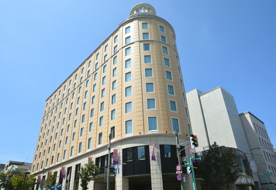 a tall , beige - colored building with a blue roof and several flags flying in front of it at Authent Hotel Otaru