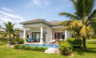 a small , white house with a swimming pool in the backyard , surrounded by lush green grass and palm trees at Melia Vinpearl Cua Sot Beach Resort