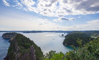 a breathtaking view of a mountainous landscape with a deep blue sea , green trees , and white clouds at Hotel Urashima