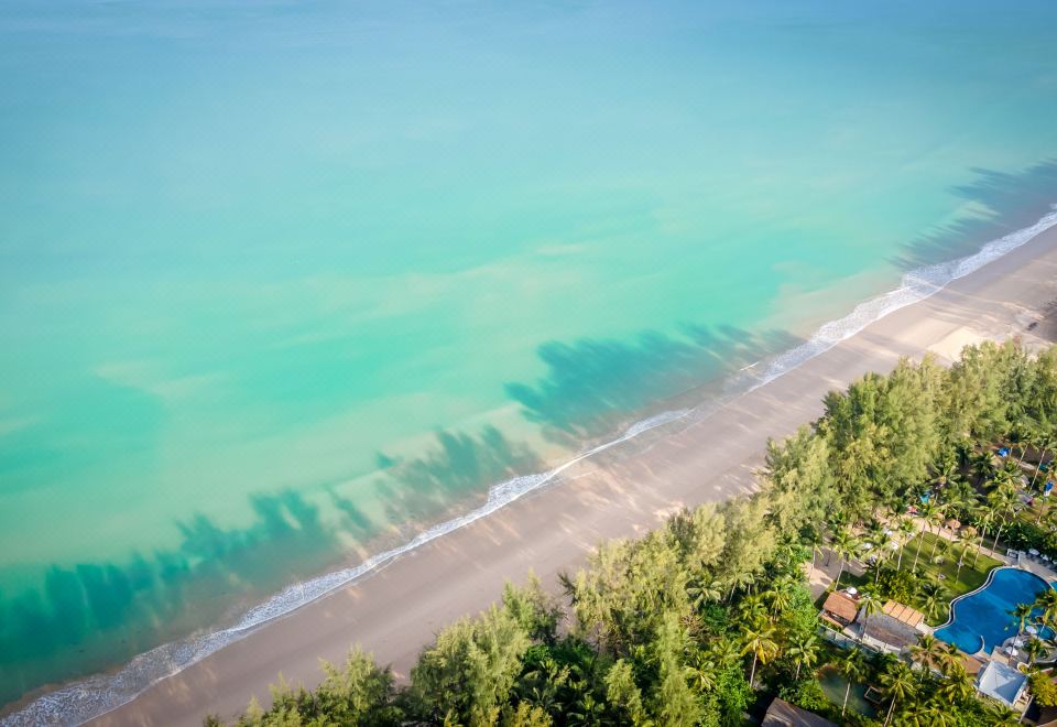 a beautiful beach with clear blue water , surrounded by lush green trees and a small island in the distance at Outrigger Khao Lak Beach Resort