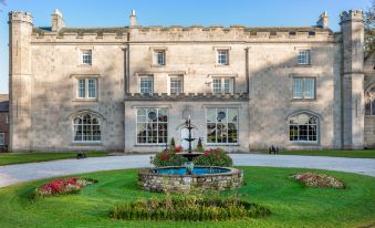 a grand stone building with a fountain in the center , surrounded by lush greenery and flowers at Thurnham Hall