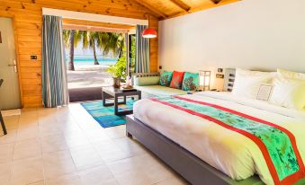 a large bed with a colorful blanket is in a room with a window and a view of the ocean at Meeru Maldives Resort Island
