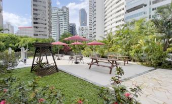 There is a patio in the center with tables and chairs, surrounded by tall buildings on both sides at Coliwoo Orchard - Co-Living Serviced Apartments